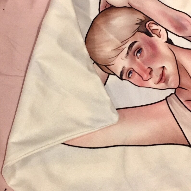 May include: A white fabric throw blanket featuring a printed illustration of a person with light brown hair, blue eyes, and flushed cheeks. The person is depicted in a reclining pose with one arm raised behind their head, rendered in a soft art style.