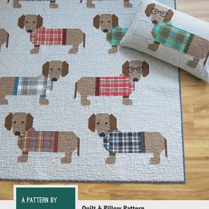 May include: A light blue quilt and pillow set featuring dachshund dogs wearing plaid sweaters and glasses. The text "DOGS IN SWEATERS" is at the top. The pattern is by Elizabeth Hartman. The quilt and pillow pattern includes instructions for making two quilt sizes.