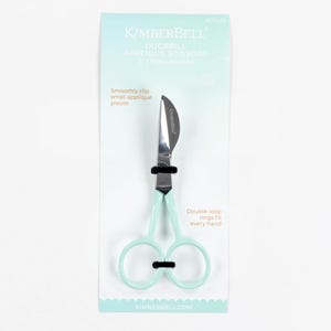 May include: Mint green Kimberbell Duckbill Applique Scissors, 5 inches long, for right-handed use. The scissors have a curved blade and double-loop rings. The packaging includes the Kimberbell logo and text that reads "Smoothly clip small applique pieces."