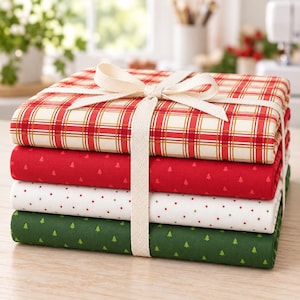 May include: A stack of four folded fabric pieces tied with a cream-colored ribbon. The top piece features a red, white, and gold plaid pattern. The second is red with small tree icons, the third is white with red and green dots, and the bottom is green with small tree icons.