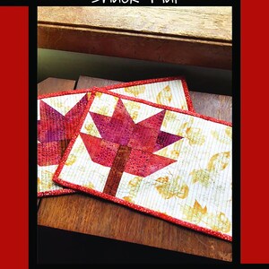 May include: Pressed Leaf Snack Mat. Two quilted snack mats with a red maple leaf design. The mats have a white background with yellow leaf patterns and red borders. The text "Pressed Leaf Snack Mat" is at the top.