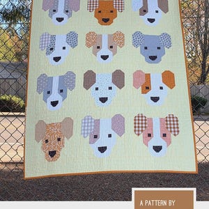 May include: A handmade quilt featuring a repeating pattern of dog faces in various colors and patterns. The quilt is on a light yellow background with a brown border. The text "THE PUPPIES" is at the top. The quilt pattern is by Elizabeth Hartman.