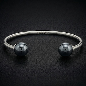 May include: A silver cuff bracelet featuring a polished, open-ended design with two large, dark, spherical beads at each terminal. The inner band of the silver metal is clearly stamped with the hallmark 925, indicating sterling silver composition.