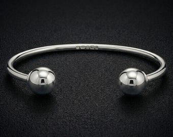 Op de afbeelding: Een gepolijste zilveren armband met een glad, open ontwerp en twee grote, bolvormige uiteinden. De binnenkant van de band is duidelijk voorzien van het keurmerk 925, wat duidt op een samenstelling van sterling zilver.