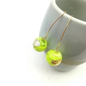 May include: A pair of gold dangle earrings with green and gold glass spheres. The spheres have a swirling pattern and gold flecks.