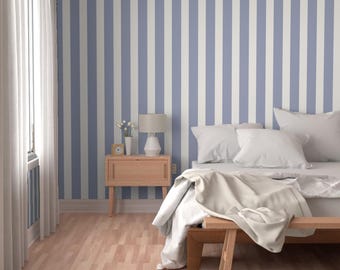 May include: A bedroom with a blue and white striped wall, a wooden nightstand with a lamp, and a bed with white bedding. The room has a light wood floor and a window with white curtains.