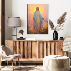 May include: A framed religious art print depicts a woman in a flowing blue robe and a white dress, surrounded by colorful flowers. The artwork has a soft, ethereal quality with a warm, golden background. The print is displayed above a wooden cabinet.