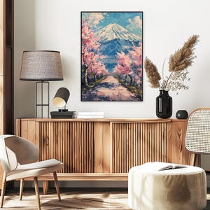 Pode incluir: Pintura emoldurada de uma paisagem montanhosa coberta de neve sob um c&eacute;u azul com nuvens. Cerejeiras em flor rosa ladeiam um caminho que leva &agrave; montanha. A obra de arte &eacute; exibida acima de um arm&aacute;rio de madeira.