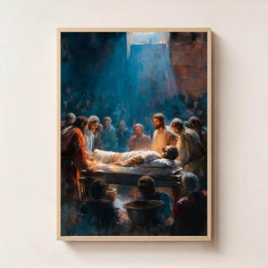 Peut inclure: Peinture encadrée représentant une scène avec des personnages rassemblés autour d'une figure allongée sur une table. L'œuvre utilise une palette de bleus, de bruns et de rouges, avec une source de lumière éclairant la figure centrale. Le style rappelle l'art classique.