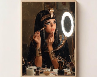 May include: A framed artwork depicts a person in ancient Egyptian attire applying makeup. The person is wearing a black and gold headdress, collar, and bracelets. A ring light illuminates the scene. Makeup brushes and products are visible on the table.