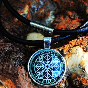 Peut inclure: Un collier en cuir noir avec un pendentif en argent orné d'un cabochon de verre circulaire avec un motif noir et blanc. Le motif comprend une boussole, des runes et d'autres symboles.