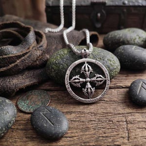May include: A silver pendant necklace with a detailed, circular design featuring a central cross-like emblem and the words "Gothic Potter" around the edge. The necklace hangs on a silver chain. The image includes leather, stones, and coins.