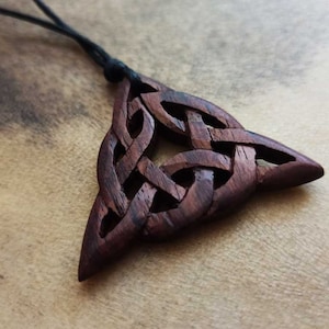 Könnte beinhalten: Ein dunkelbrauner Holzanhänger mit einem keltischen Knotendesign in Form eines Dreiecks.