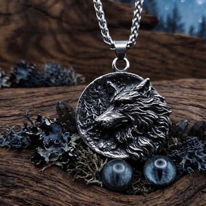 Könnte beinhalten: Silberfarbene Halskette mit einem Anhänger, der einen detaillierten Wolfskopf zeigt. Der runde Anhänger hängt an einer Kette. Das Bild enthält dekorative Elemente wie Kristalle und blau-graue Kugeln, vor einem rustikalen Holzgrund.