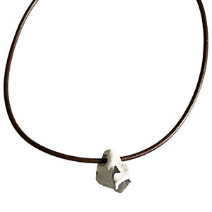 May include: A brown leather cord necklace with a silver pendant shaped like a rough, irregular rock.