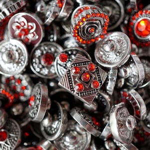 May include: A close-up of a pile of silver and red buttons with rhinestones. The buttons are various shapes and sizes, with some having intricate designs.