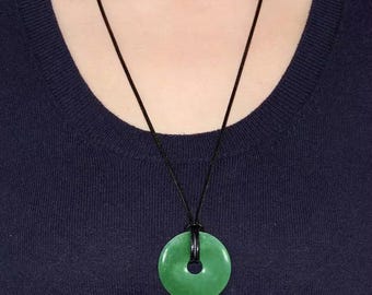 May include: A green jade pendant necklace with a black leather cord. The pendant is a round disc with a hole in the center.