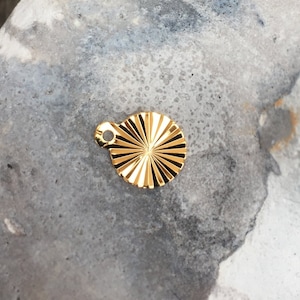 Peut inclure: Un charme en métal doré avec un motif en forme de soleil. Le charme est rond et a une surface texturée.