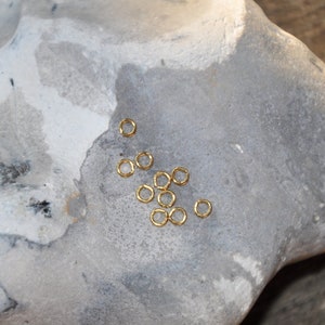May include: A gray stone with a cluster of small gold jump rings scattered on its surface.