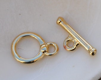 May include: Gold-toned metal toggle clasp with a round ring and a bar with a small loop. The clasp is used for jewellery making.