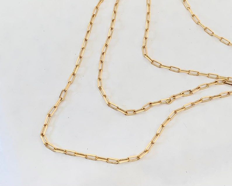 May include: A gold chain necklace with a delicate, linked design. The chain is made of small, rectangular links.