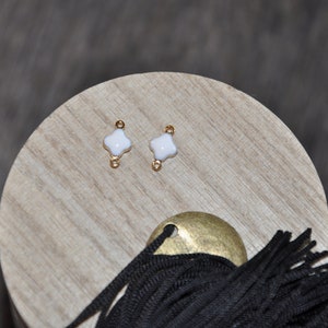 Puede incluir: Dos conectores de metal dorado con abalorios de tr&eacute;bol de cuatro hojas de esmalte blanco. Los abalorios miden aproximadamente 1 cm de di&aacute;metro.
