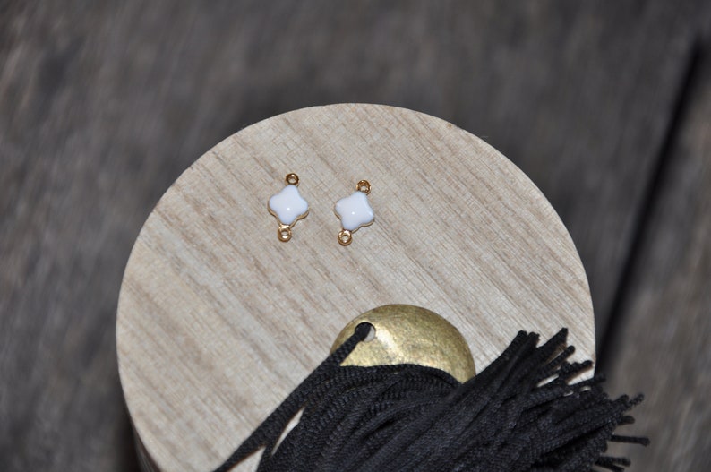 Puede incluir: Dos conectores de metal dorado con abalorios de tr&eacute;bol de cuatro hojas de esmalte blanco. Los abalorios miden aproximadamente 1 cm de di&aacute;metro.