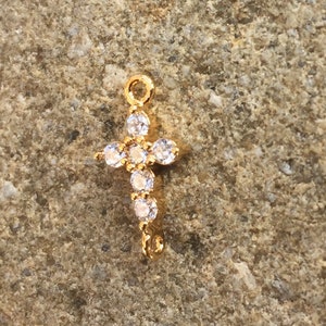 May include: Gold-tone cross charm with clear crystal accents. The charm has a loop at the top for attaching to a necklace or bracelet.