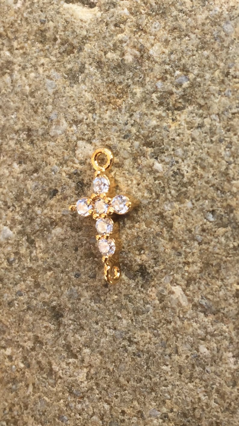 May include: Gold-tone cross charm with clear crystal accents. The charm has a loop at the top for attaching to a necklace or bracelet.