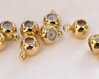 May include: A collection of gold-colored, round jewelry beads with a small loop and a white interior. These beads are likely used for jewelry making, such as necklaces or bracelets. The beads are shown on a white surface.