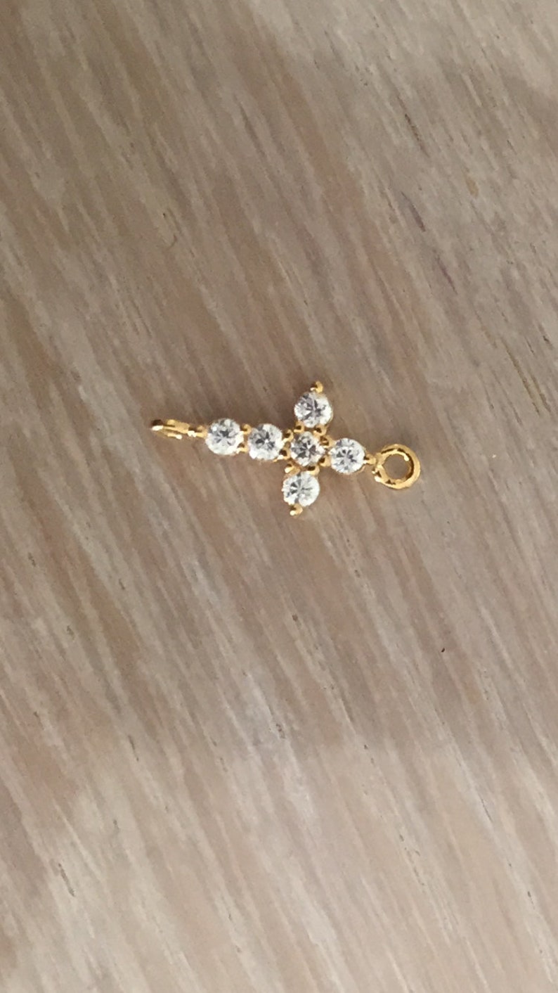 May include: A gold cross charm with clear cubic zirconia stones.