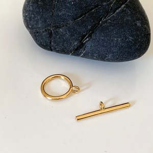 Puede incluir: Dos cierres de joyer&iacute;a de metal dorado. Uno es un anillo redondo con un peque&ntilde;o bucle en el lateral. El otro es una barra recta con un bucle en un extremo.