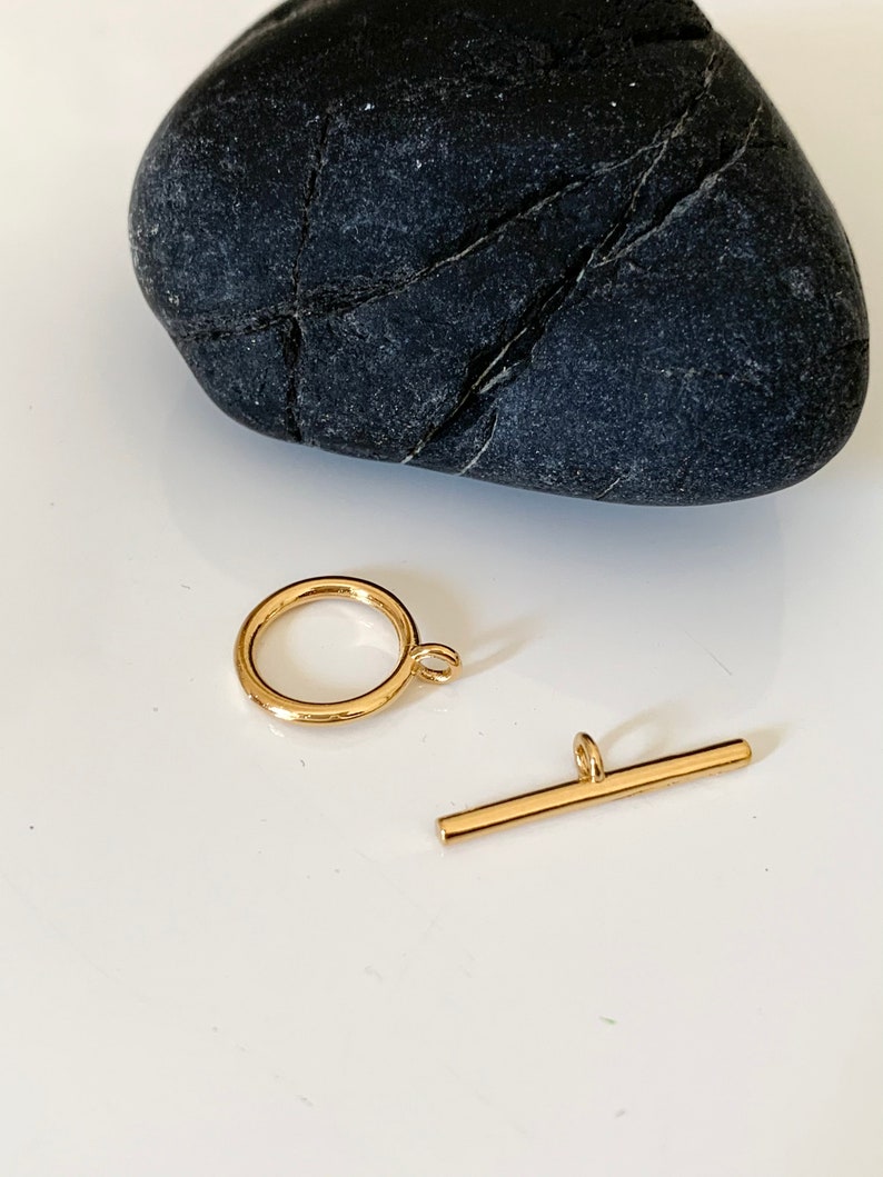 Puede incluir: Dos cierres de joyer&iacute;a de metal dorado. Uno es un anillo redondo con un peque&ntilde;o bucle en el lateral. El otro es una barra recta con un bucle en un extremo.