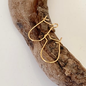 Könnte beinhalten: Ein Paar goldfarbene Creolen mit einem einfachen, geschwungenen Design. Die Ohrringe werden auf einem Stück Treibholz präsentiert.