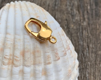 May include: Gold-toned metal clasp with a spring-loaded closure. The clasp is designed for attaching to a chain or cord.