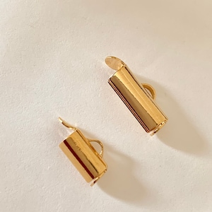 Peut inclure: Deux fermoirs en métal doré pour la fabrication de bijoux. Chaque fermoir a une forme cylindrique avec une petite boucle à une extrémité et une extrémité arrondie plate à l'autre.