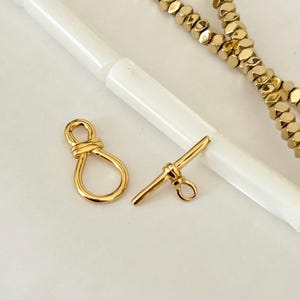 以下が含まれることがあります： ジュエリー作りのための2つの金色の金属製留め具。1つの留め具はループ付きのシンプルなバーで、もう1つは8の字形です。