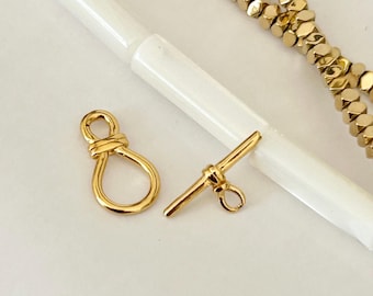 May include: Two gold-toned metal clasps for jewellery making. One clasp is a simple bar with a loop, the other is a figure eight shape.