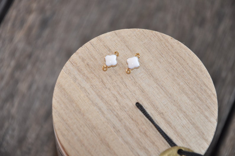 Puede incluir: Dos encantos de tr&eacute;bol de cuatro hojas de esmalte blanco con anillos de salto de tono dorado.