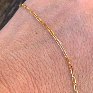 May include: A gold chain necklace with a delicate, box chain design. The chain is made of small, rectangular links that are connected together to create a smooth, continuous chain.
