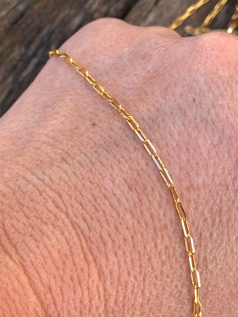 May include: A gold chain necklace with a delicate, box chain design. The chain is made of small, rectangular links that are connected together to create a smooth, continuous chain.