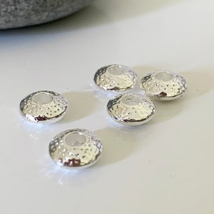 以下が含まれることがあります： 中央に穴があり、表面がテクスチャ加工された銀色の金属ビーズが5つあります。ビーズは丸くて平らです。