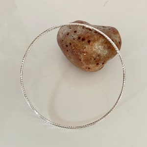 Peut inclure: Un bracelet jonc en argent avec un design torsadé. Le bracelet est sur une surface blanche.