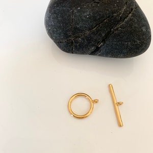 Puede incluir: Cierre de palanca de metal dorado con un anillo redondo y una barra recta. El cierre es un hallazgo de joyer&iacute;a para collares, pulseras u otros proyectos de joyer&iacute;a.