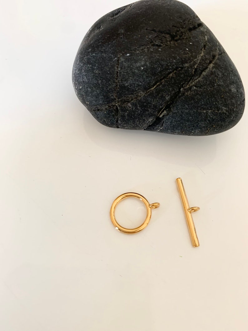 Puede incluir: Cierre de palanca de metal dorado con un anillo redondo y una barra recta. El cierre es un hallazgo de joyer&iacute;a para collares, pulseras u otros proyectos de joyer&iacute;a.