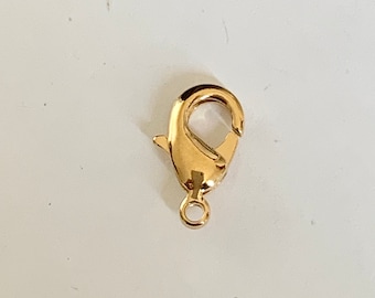 Könnte beinhalten: Goldfarbener Metall-Hummerverschluss mit federndem Verschluss. Der Verschluss ist zum Anbringen von Schmuck oder anderen Accessoires gedacht.