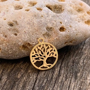 Könnte beinhalten: Ein goldfarbener Metallanhänger in Form eines Lebensbaums. Der Anhänger ist rund und hat ein detailliertes Design eines Baumes mit Ästen und Wurzeln.