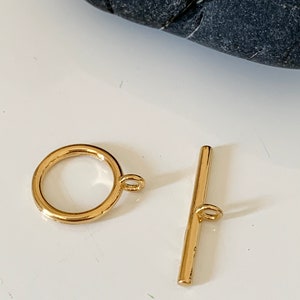 Puede incluir: Cierre de palanca de metal dorado con un anillo redondo y una barra recta. El cierre se utiliza para la fabricaci&oacute;n de joyas.