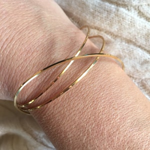 May include: Three gold bangle bracelets stacked on a wrist. The bracelets are thin and have a smooth, polished finish.