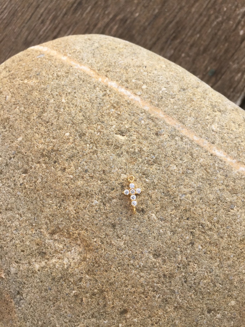 May include: A small gold cross charm with clear sparkling rhinestones.
